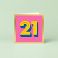 olourful 21st birthday card with large yellow number 21, blue shadow detail, bright pink background and gold foil border.