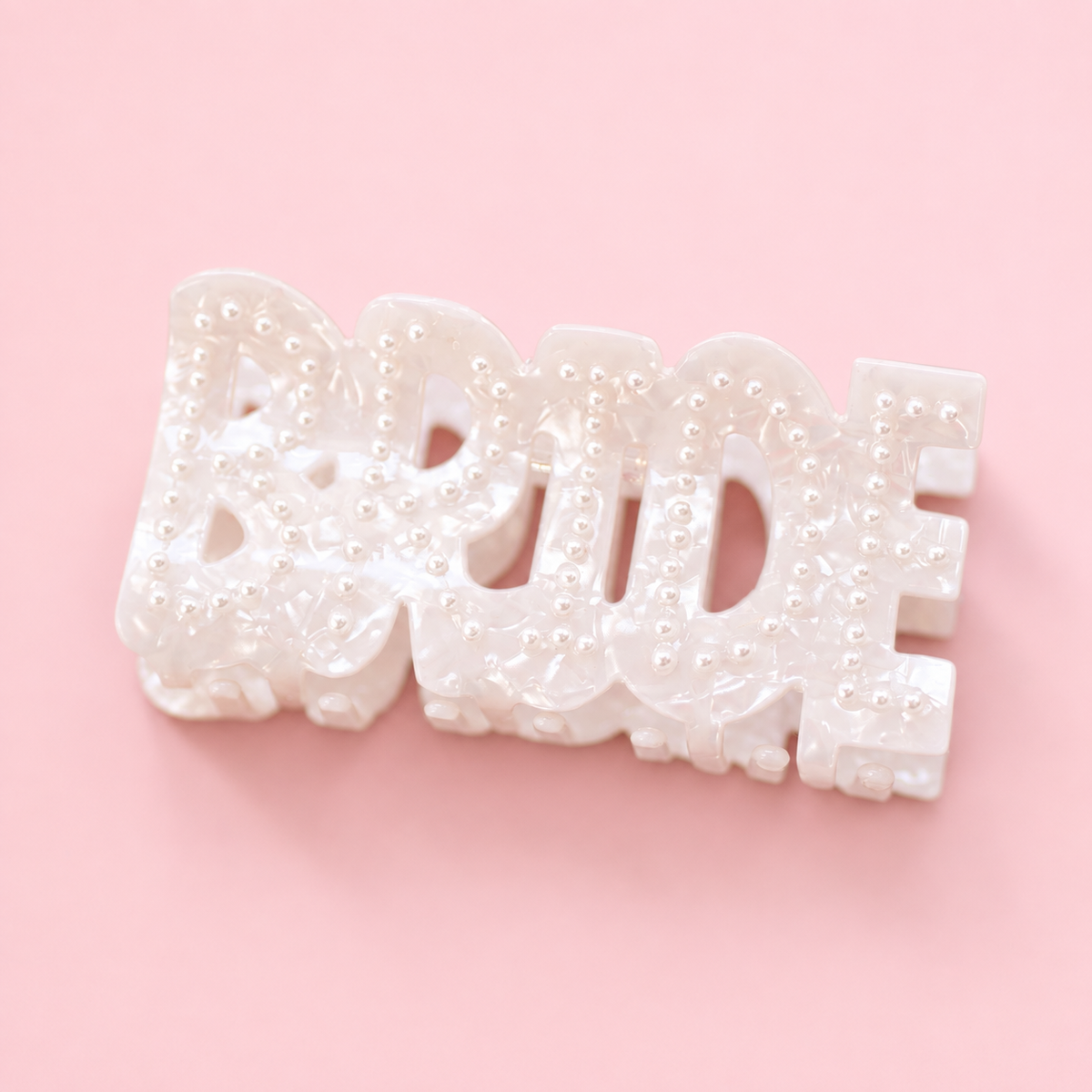 Pearlescent white BRIDE claw hair clip decorated with small pearl details on a soft pink background.