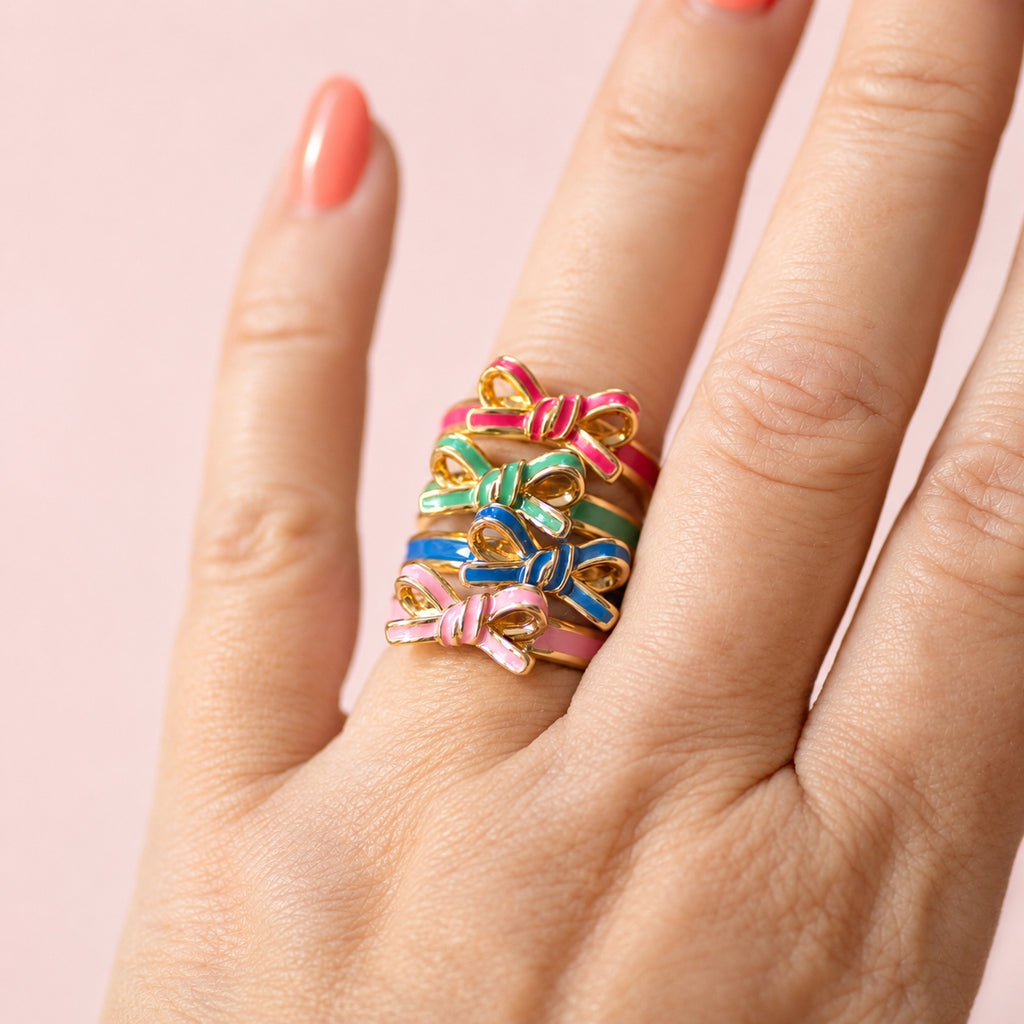 Colourful enamel bow rings stacked together in pink, green and blue with slim gold-tone bands.