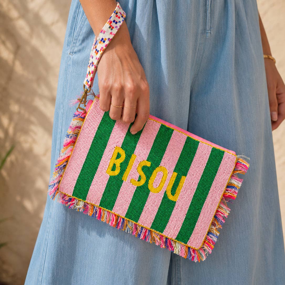 Pink and green striped beaded Bisou clutch bag with colourful fringe and wrist strap, carried by hand.