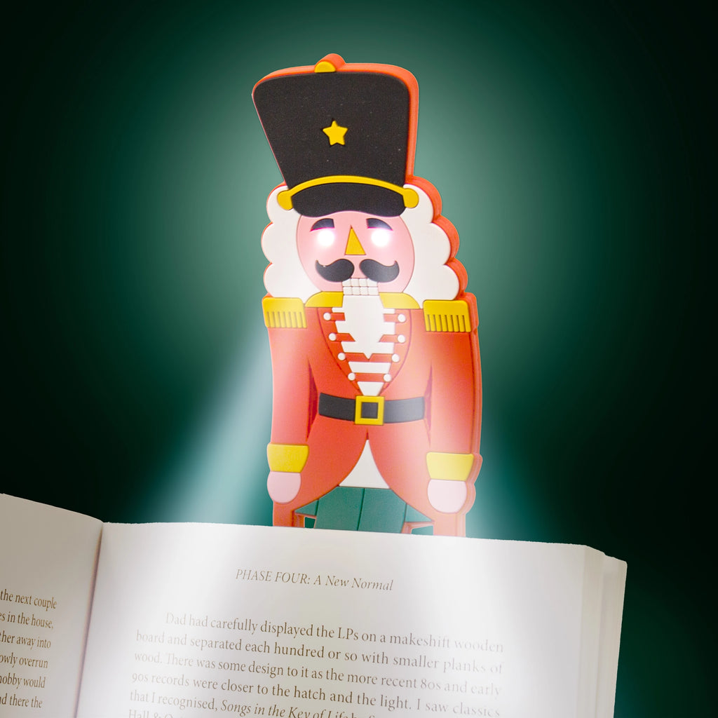 Nutcracker reading light glowing over the pages of an open book in the dark.