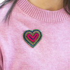 Pink and green beaded heart brooch pinned to a pink knitted jumper.