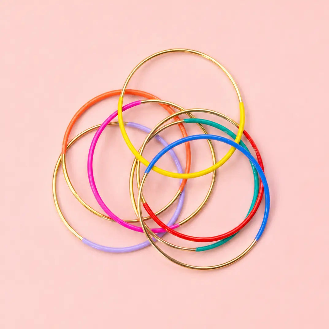 Collection of colourful gold tone dip enamel stacking bangles in assorted enamel colours on a pale pink background.