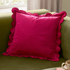 Hot pink velvet cushion with playful scalloped edging styled on an olive green sofa.