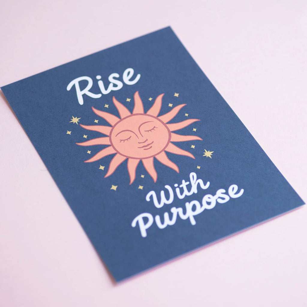 Colourful Rise With Purpose art print featuring a peaceful peach sun and golden stars, photographed against a soft pink background.