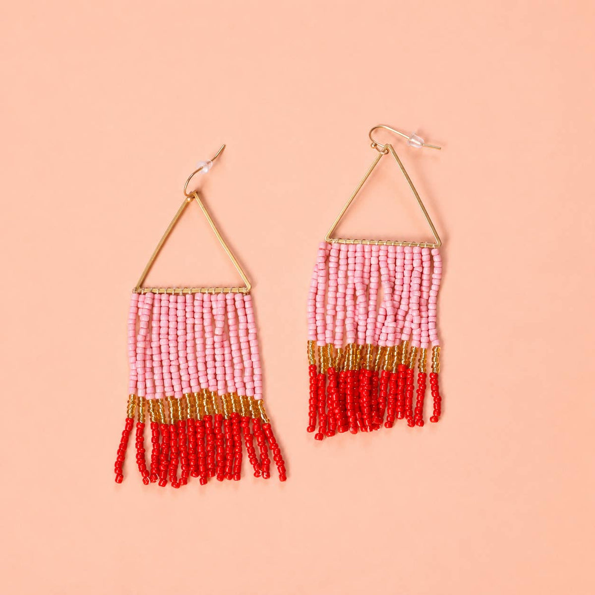 Pair of pink, red and gold beaded fringe earrings with triangular gold tone frames on a peach background.