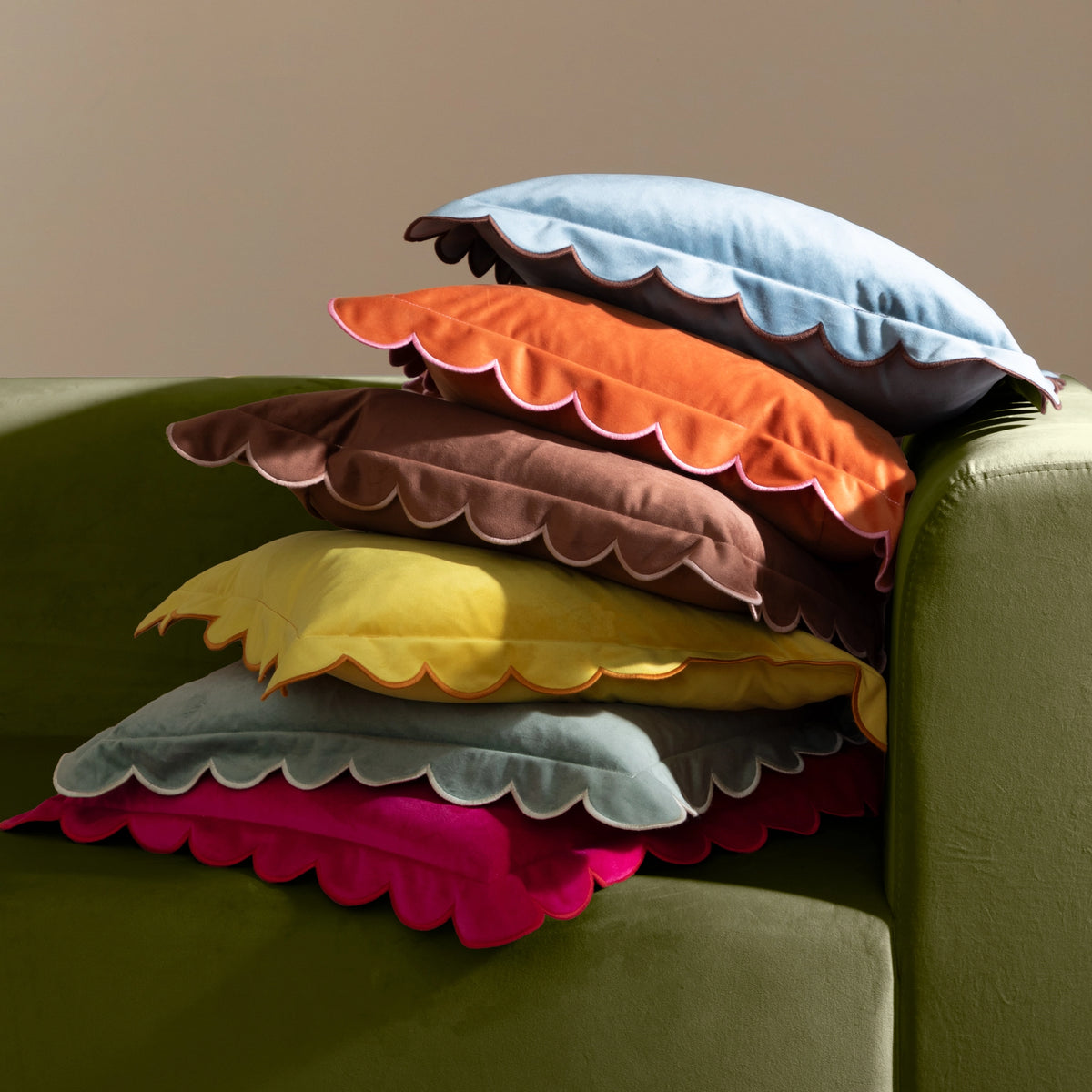 Stack of colourful scalloped velvet cushions in orange, blue, brown, yellow, green and pink.