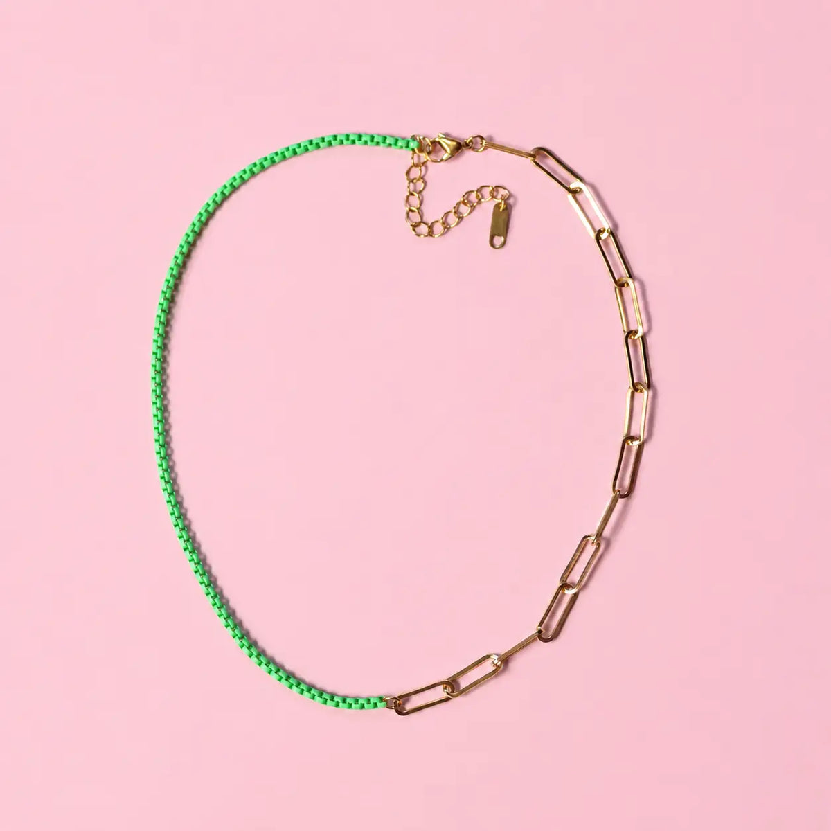 A hybrid chain necklace featuring a vibrant green beaded section and a gold paperclip chain section, displayed on a solid pink background.
