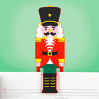 Colourful Nutcracker bookmark clipped over the top of an open book against a green background.