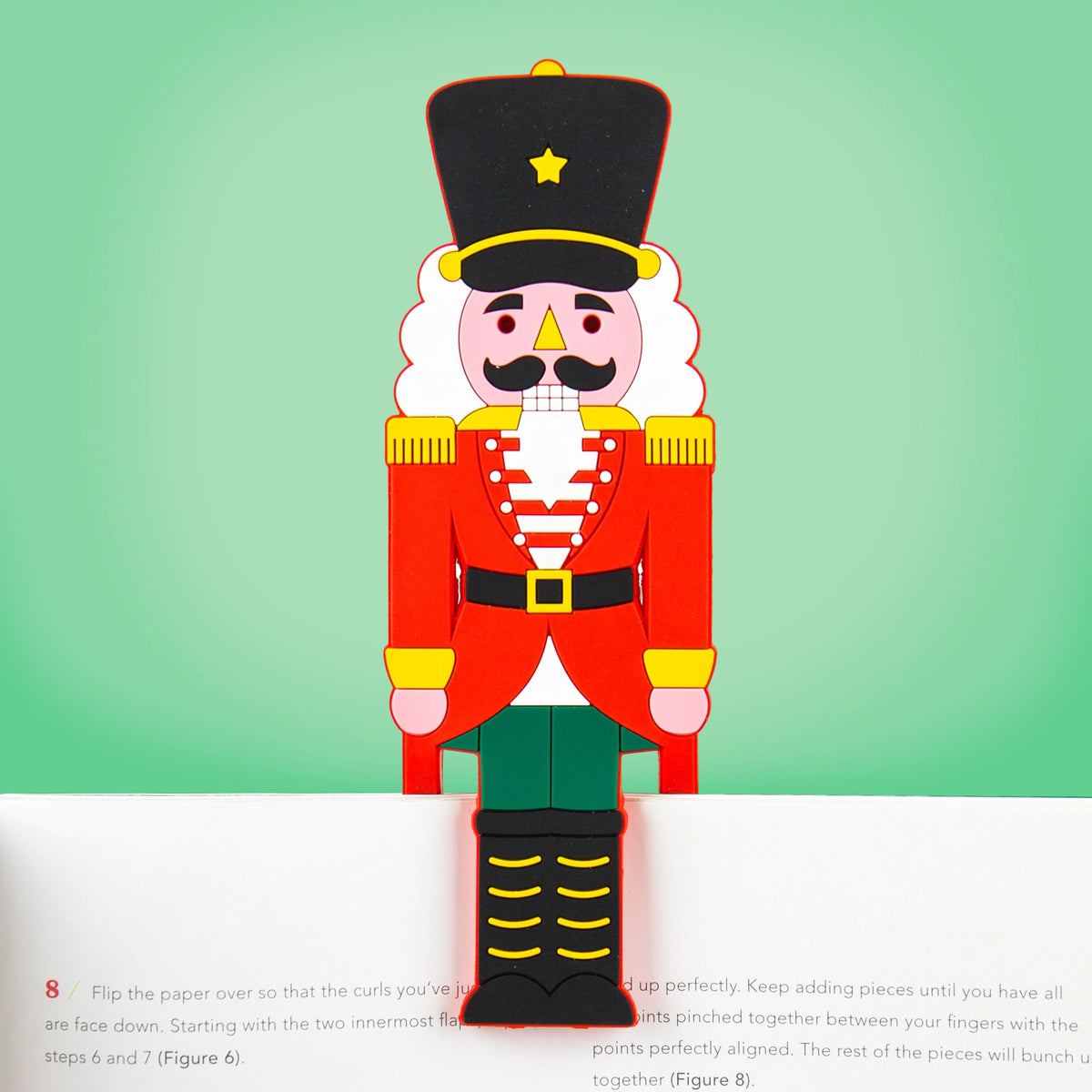Colourful Nutcracker bookmark clipped over the top of an open book against a green background.