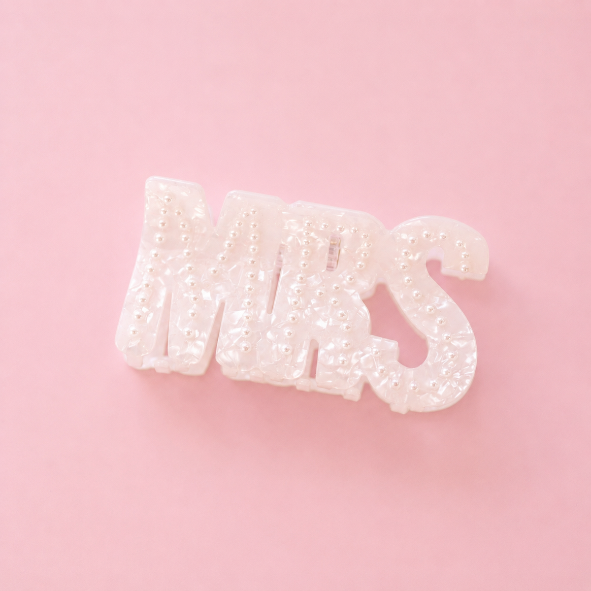 Pearlescent white MRS claw hair clip decorated with small pearl details on a soft pink background.