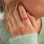 Pink enamel bow ring with a slim gold-tone band worn on the hand for a playful everyday jewellery look.