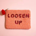 Coral pink beaded zip pouch with red sequin ‘LOOSEN UP’ lettering and red pom pom zip detail.