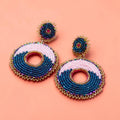 Pink and navy circular beaded statement earrings with gold detailing on a peach background.