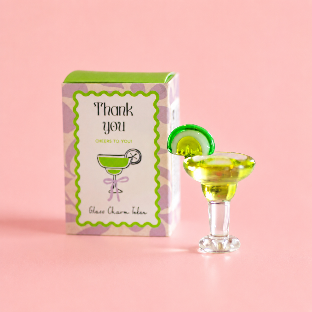 Thank You glass margarita token with green lime detail beside its colourful gift box on a soft pink background.