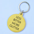 Gold ound keyring with black Less Bitter More Glitter lettering and silver key ring.