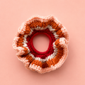 One-of-a-kind Pumpkin Spice crochet scrunchie in orange, cream, pink and raspberry on a peach background.
