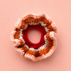 One-of-a-kind Pumpkin Spice crochet scrunchie in orange, cream, pink and raspberry on a peach background.