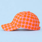 Fun pink and orange polka dot baseball cap shown from the side with its curved peak and adjustable fastening.