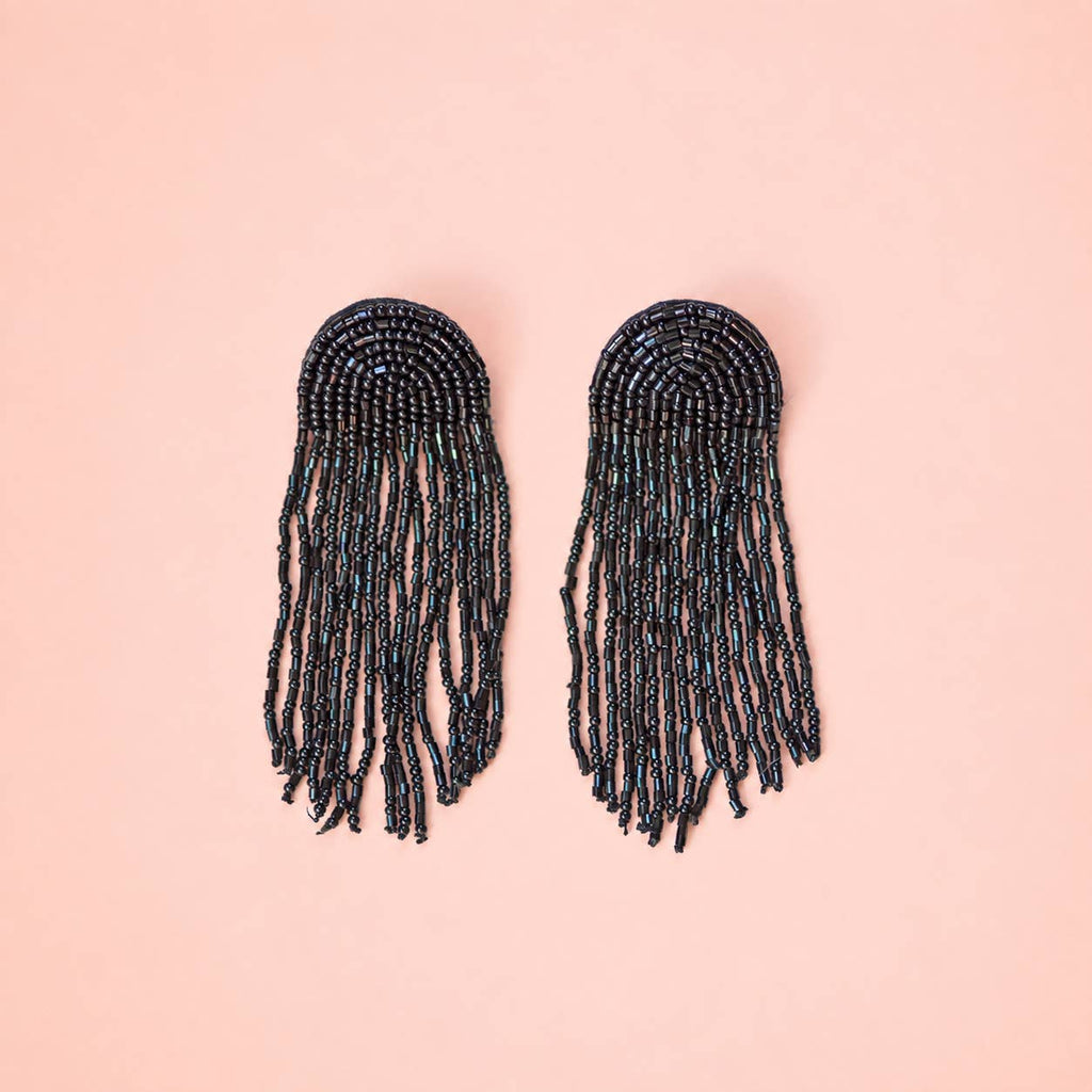 Pair of black beaded fringe statement earrings with rounded tops and long cascading strands on a pink background.