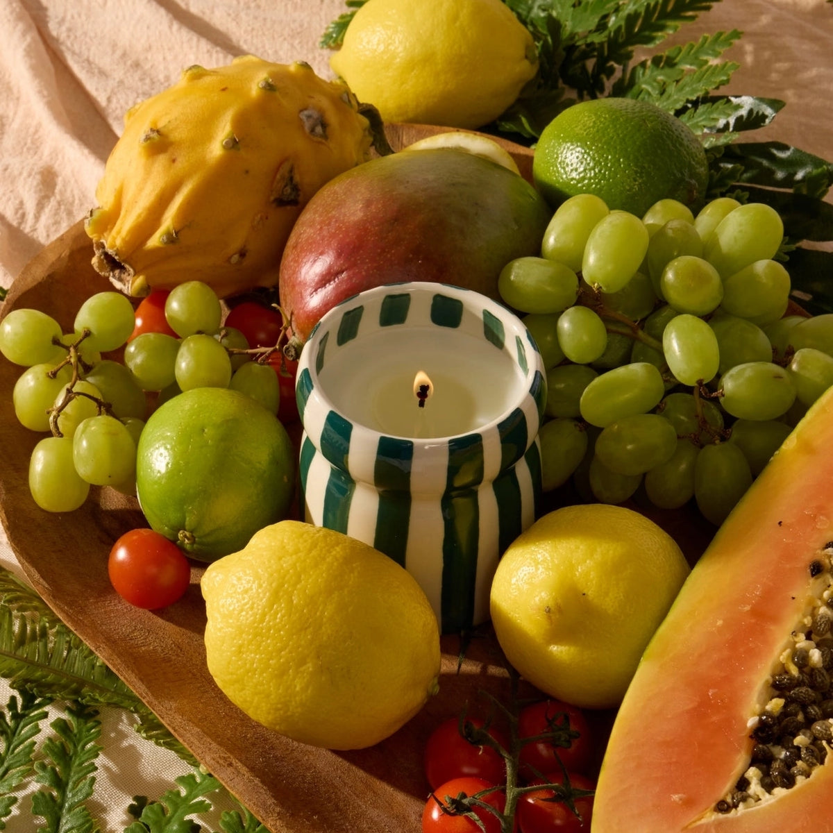 Lit Isla Fresa green and cream striped ceramic candle styled amongst colourful fresh fruit.
