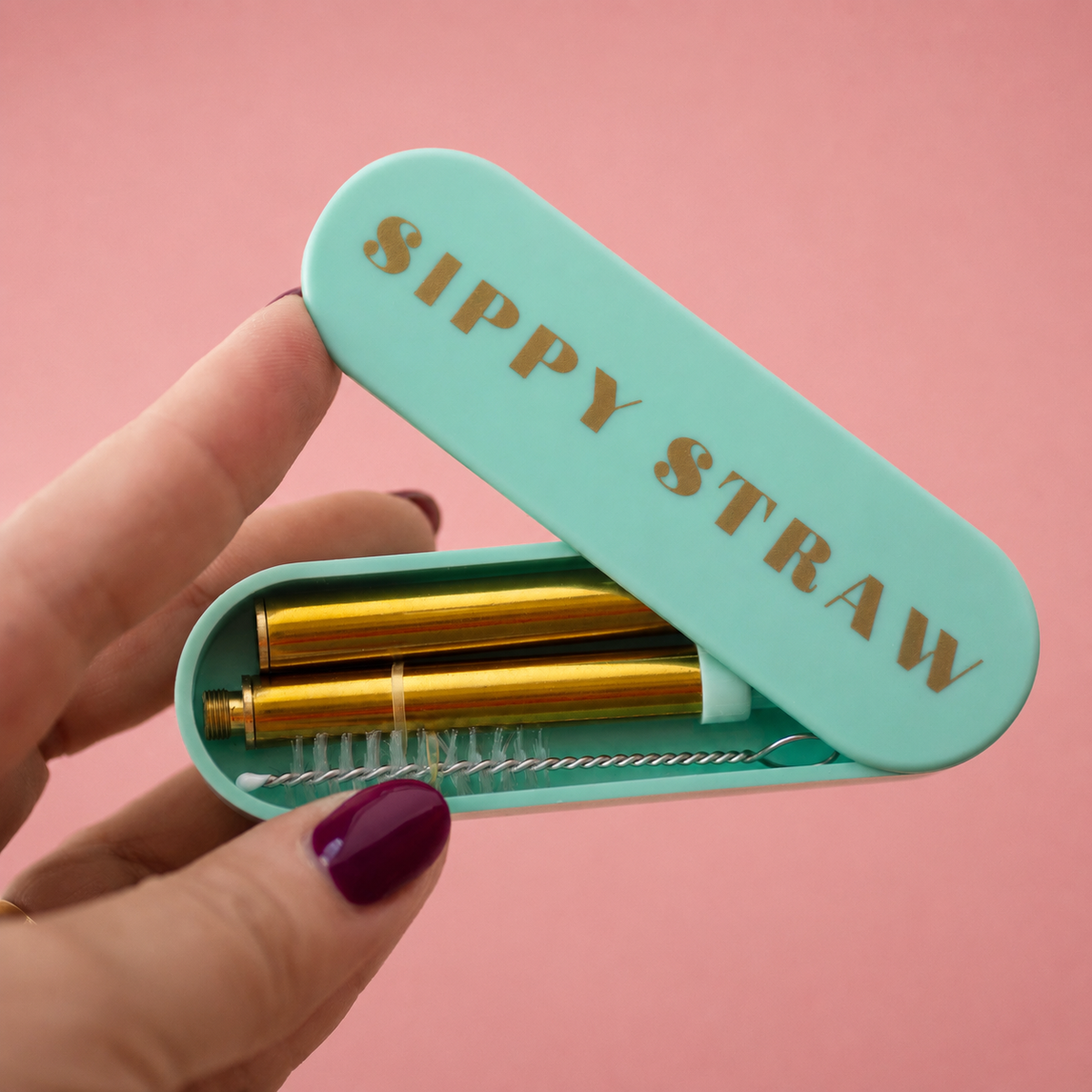 Mint green Sippy Straw travel case held open to show a gold coloured reusable straw and cleaning brush inside