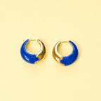 Cobalt blue enamel huggie hoop earrings with polished gold-tone detailing displayed on a yellow background.