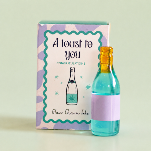 Colourful glass bottle token in turquoise, lilac and gold beside its A Toast To You congratulations gift box.
