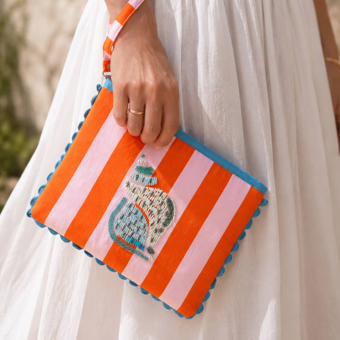Joyful orange and pink striped clutch with blue trim and a beaded shell design, carried by its wrist strap.