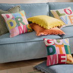 Colourful Good Times tufted cushion styled with bright cushions on a pale blue sofa.