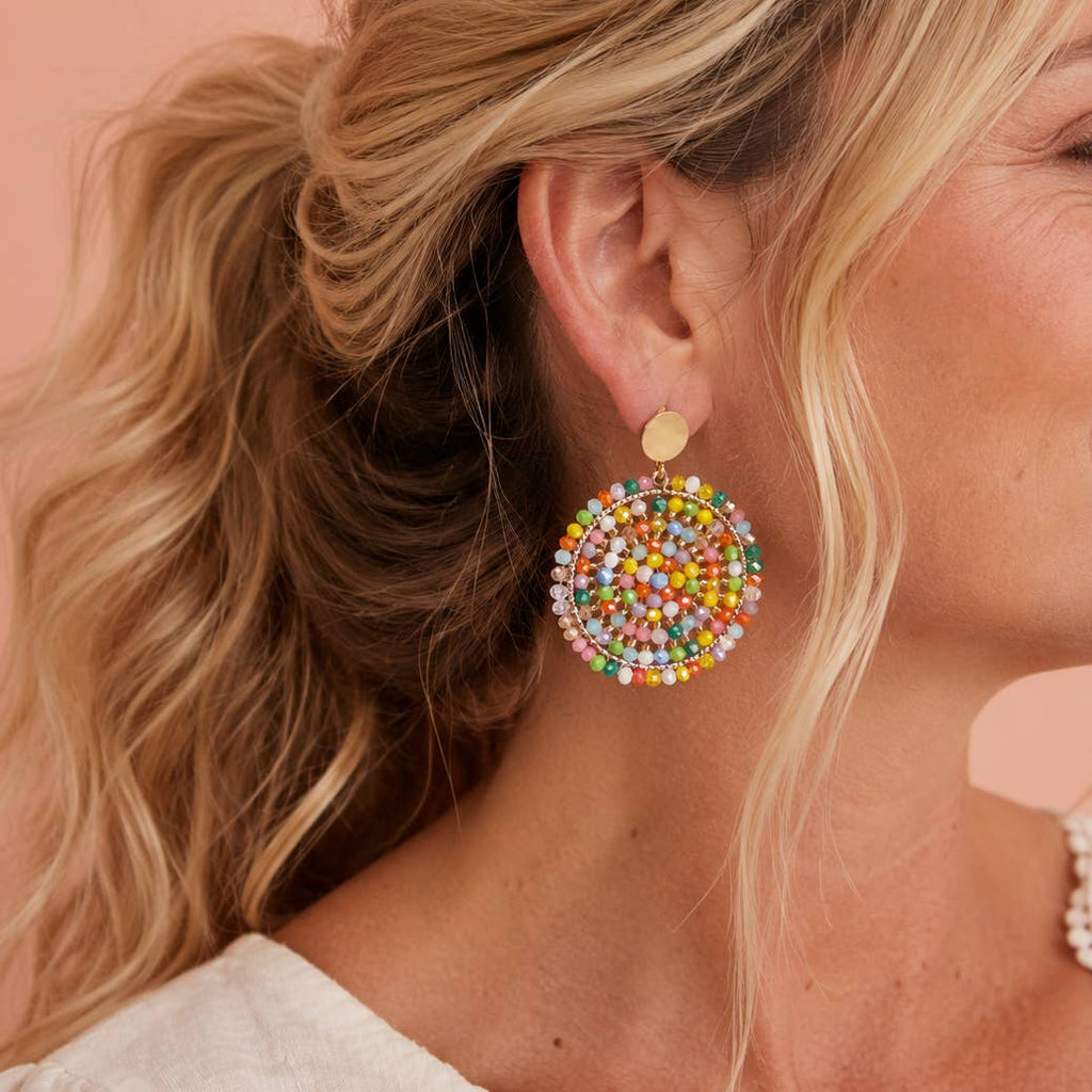Colourful beaded circular statement earring with gold tone stud worn on the ear.