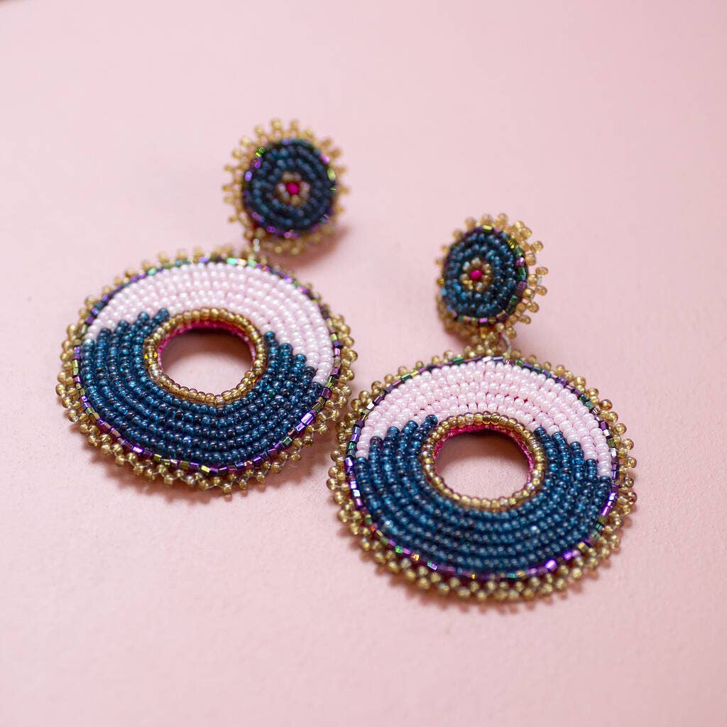Pair of pink and navy circular beaded drop earrings displayed on a pale pink background.
