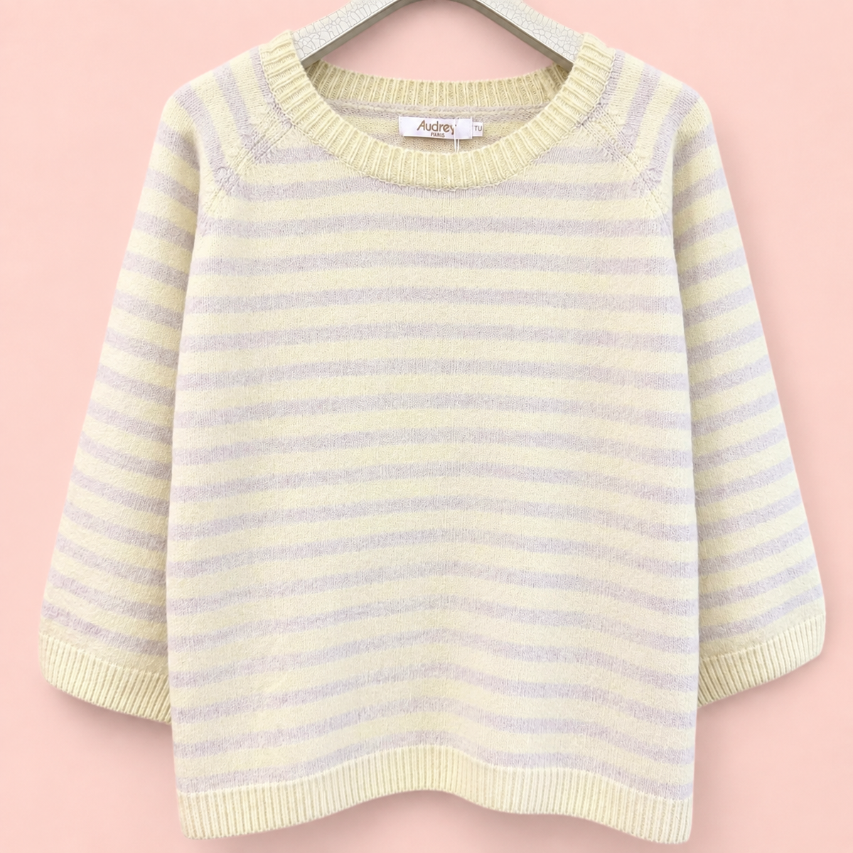 Soft lemon and pale grey striped three quarter sleeve knitted jumper on a hanger against a pink background.
