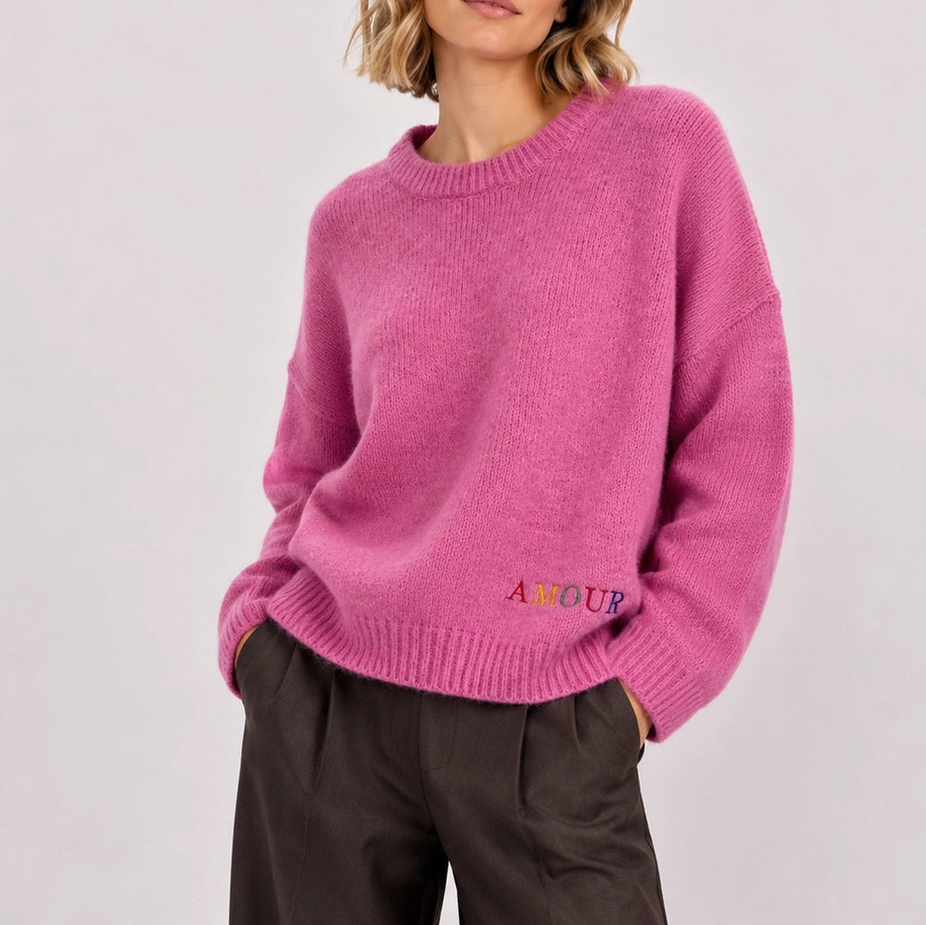 Woman wearing relaxed pink knitted AMOUR jumper showing the small embroidered detail at the front.