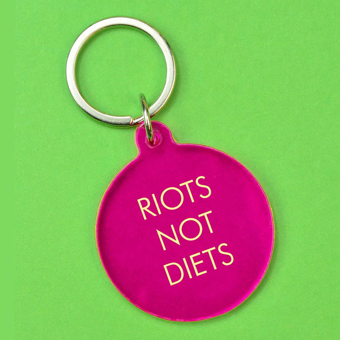 Hot pink round statement keyring with pale yellow Riots Not Diets lettering and silver-tone metal keyring attachment.