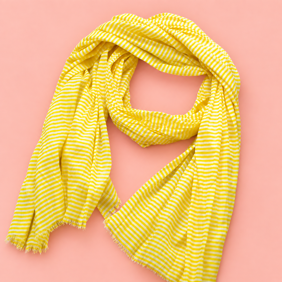 Lightweight yellow and white striped cotton scarf with softly frayed edges on a peachy pink background.