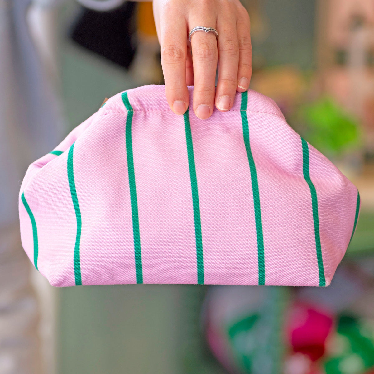 Bright pink clutch bag with fresh green stripes held up to show its roomy, softly structured shape.
