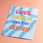 Colourful Love Dream And Stay Weird A5 print displayed on a peach background with bold retro typography.