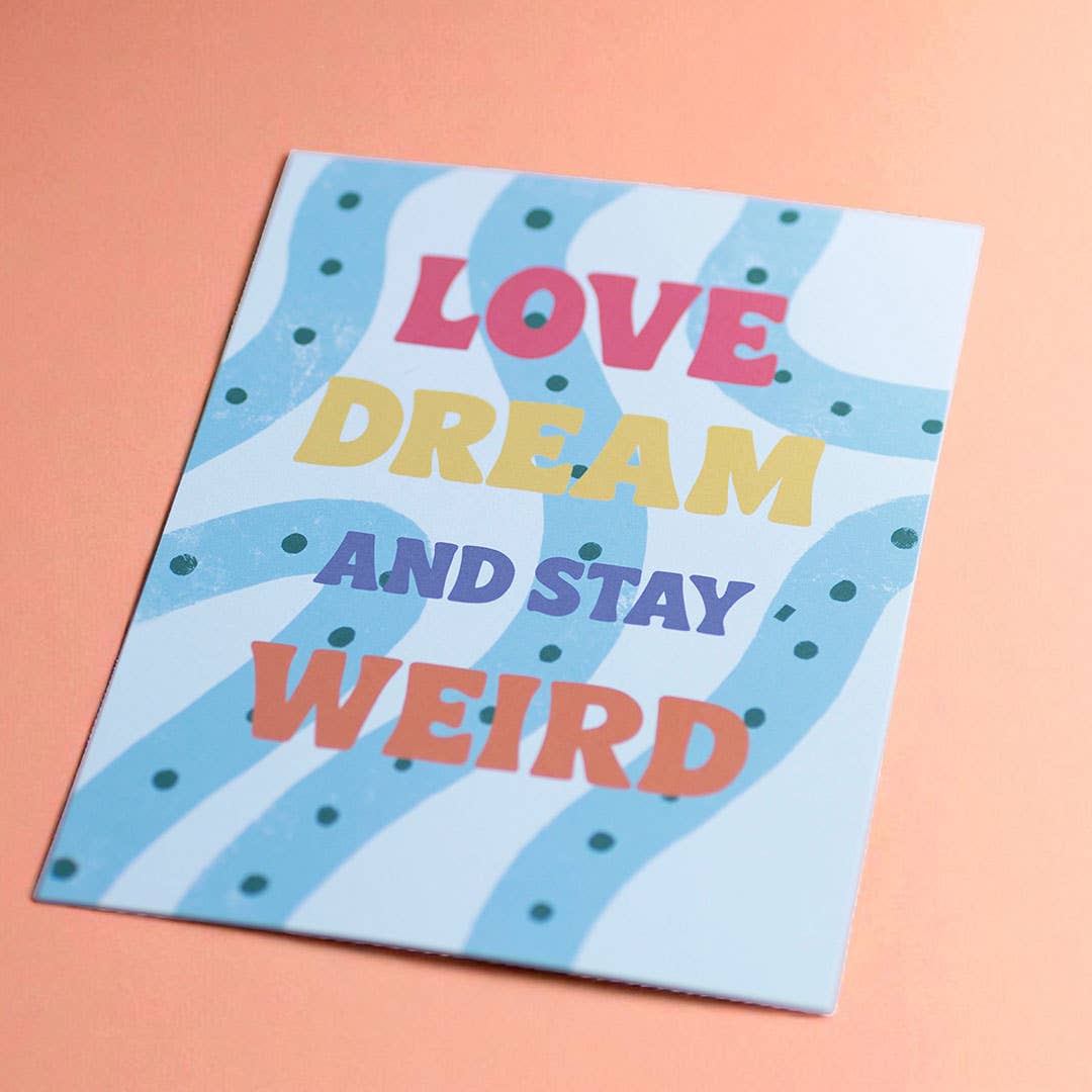 Colourful Love Dream And Stay Weird A5 print displayed on a peach background with bold retro typography.