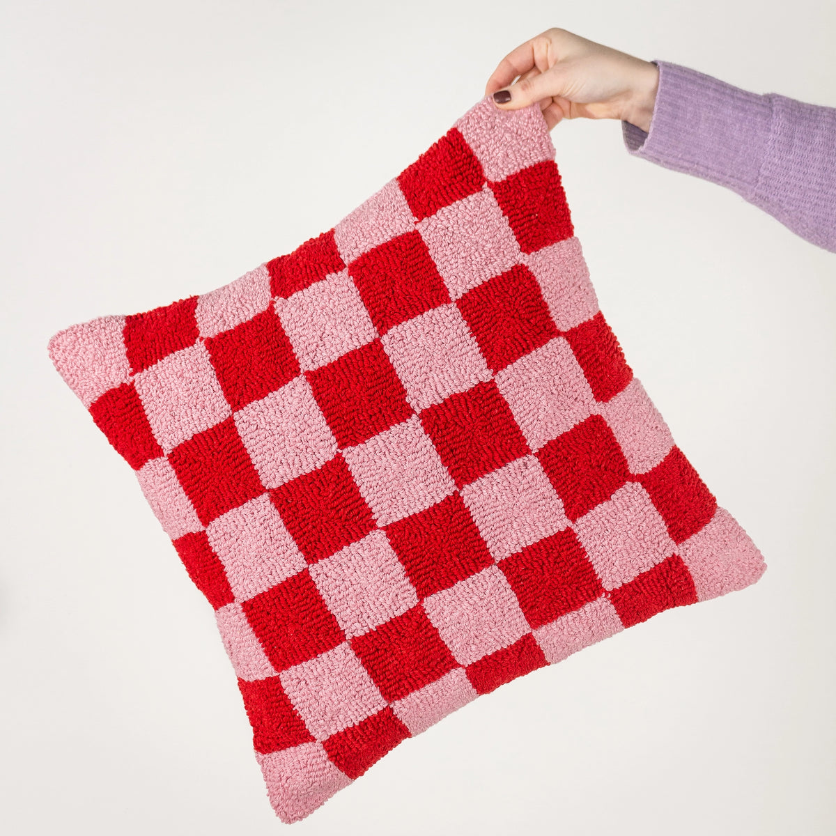 Pink and bright red checkerboard tufted cushion held by hand against a neutral background.