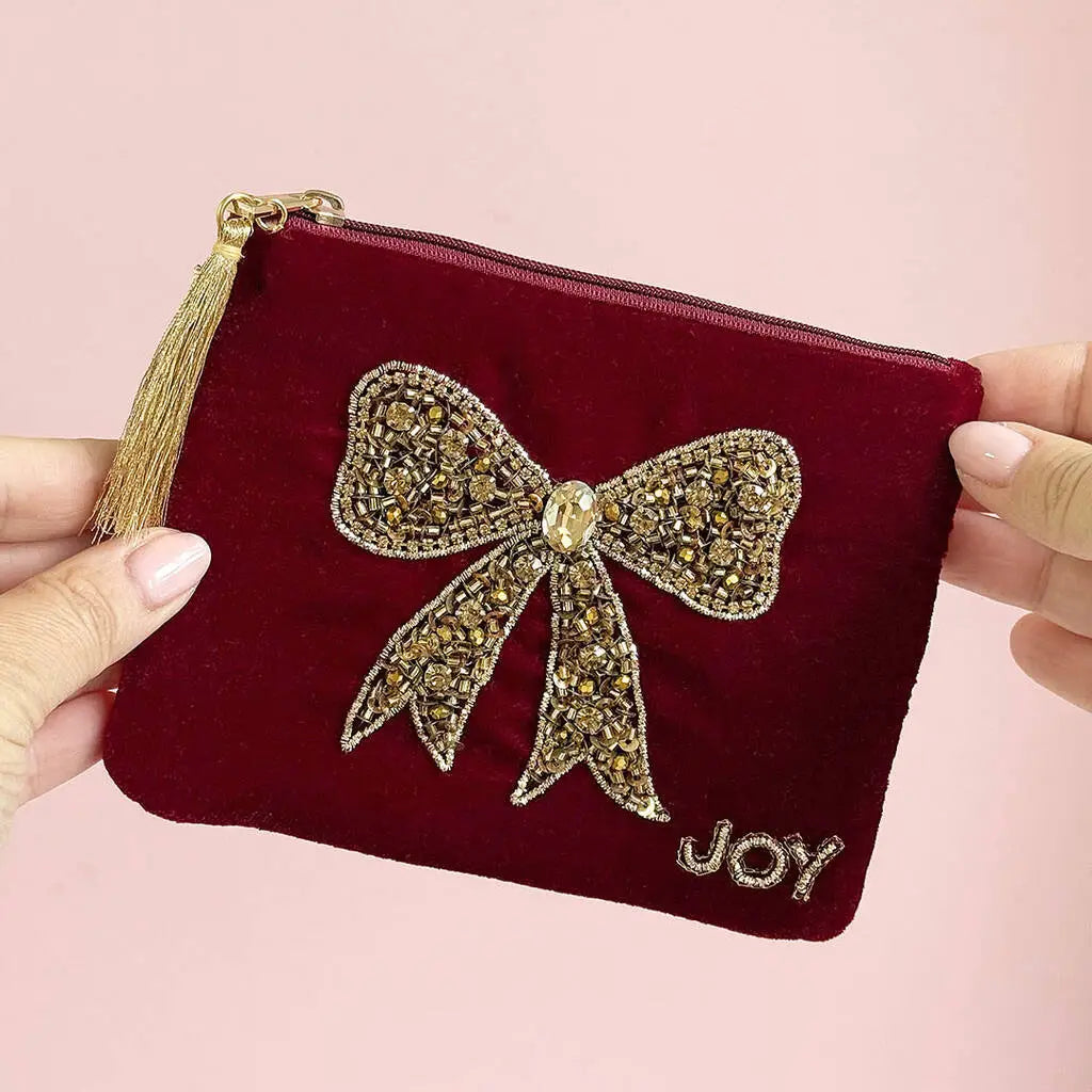 Red velvet zip pouch with hand beaded gold bow, embroidered ‘Joy’ detail and gold tassel zip pull.