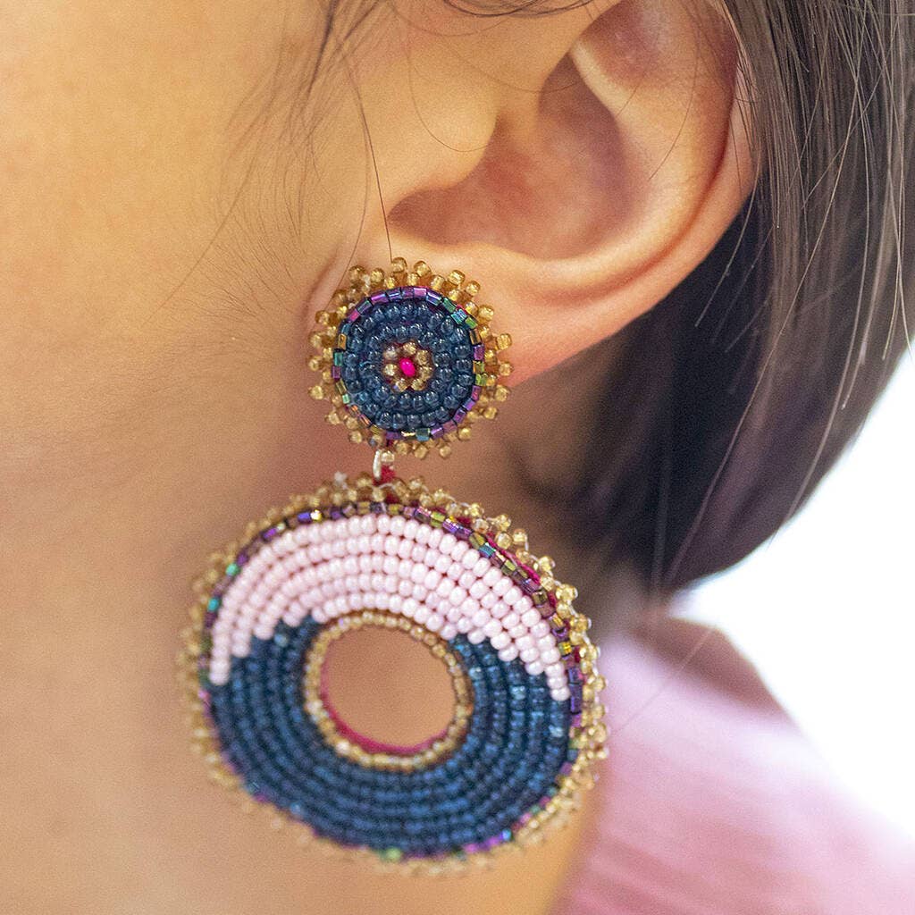 Pink and navy circular beaded statement earring worn on the ear, showing the large drop design.