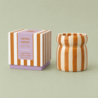 Sienna Sunset soy wax candle in a caramel and cream striped ceramic vessel beside its matching striped box.