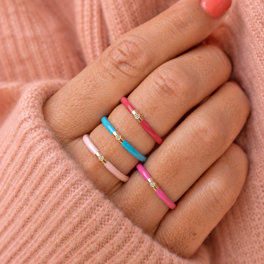 Colourful enamel CZ rings in pale pink, turquoise and pink worn stacked across a woman’s fingers.