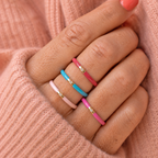 Colourful enamel CZ rings in pale pink, turquoise and pink worn stacked across a woman’s fingers.
