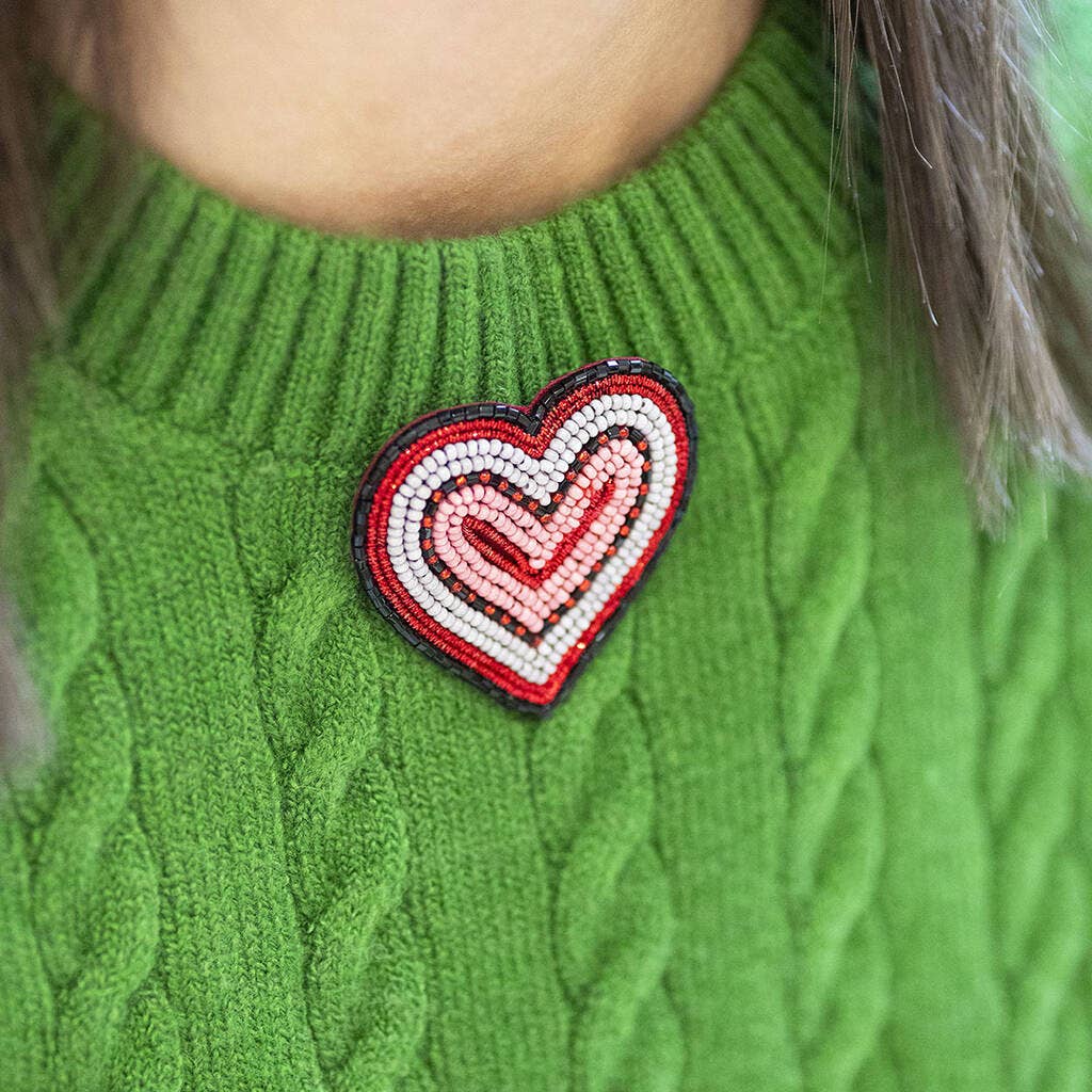 Red and pink beaded heart brooch pinned to a bright green knitted jumper.