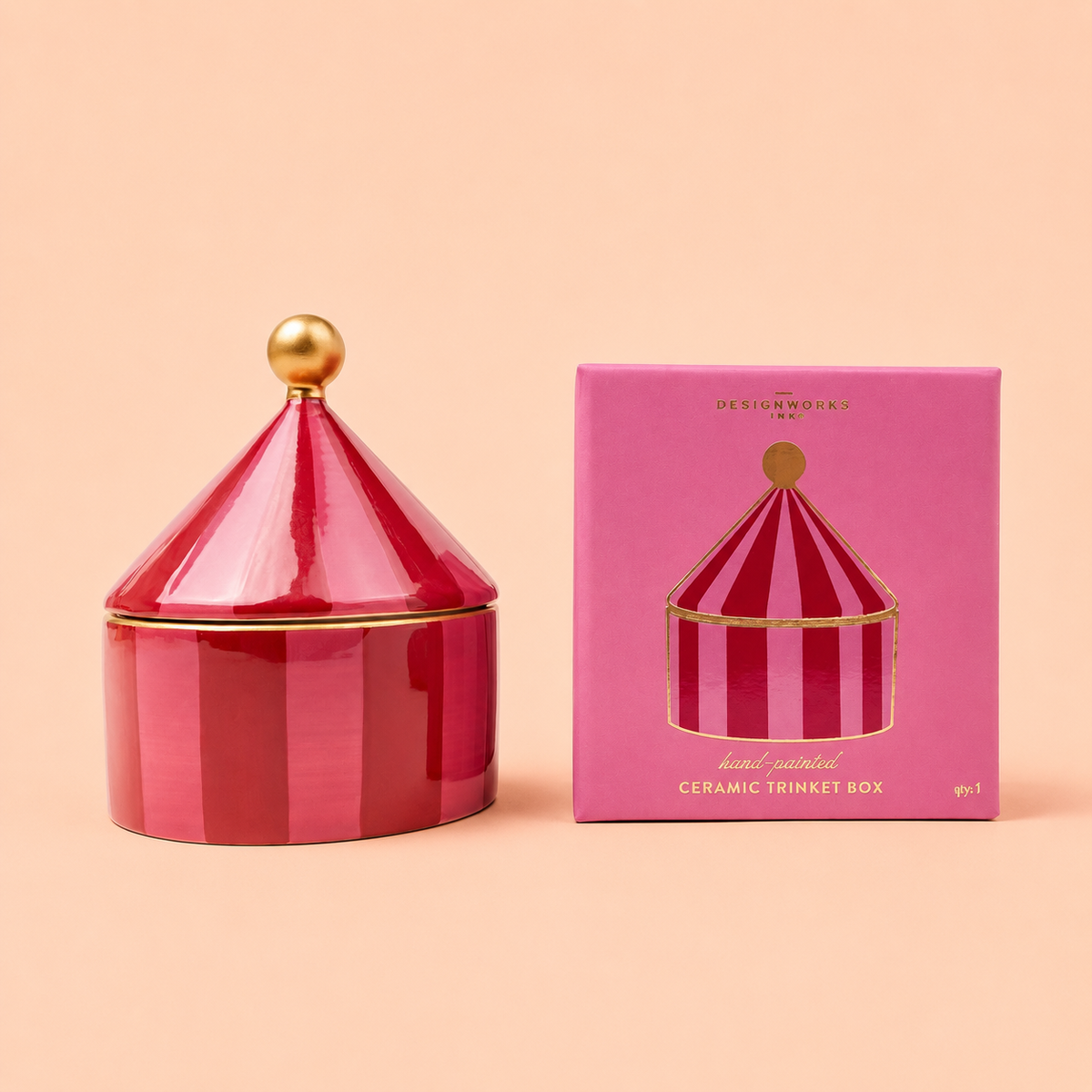 Pink and red striped hand painted ceramic trinket box with pointed lid and gold coloured details beside its pink packaging.
