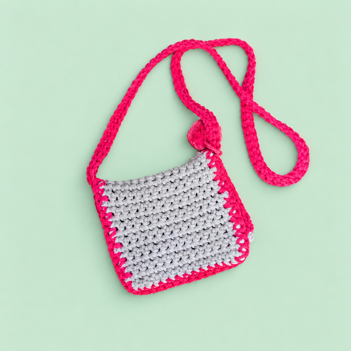 One of a kind pale blue and raspberry crochet crossbody bag handmade by Corrine in heavyweight macramé yarn with pom pom.