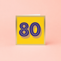 Colourful 80th birthday card with large purple number 80 on a bright yellow background with gold foil detailing and border.