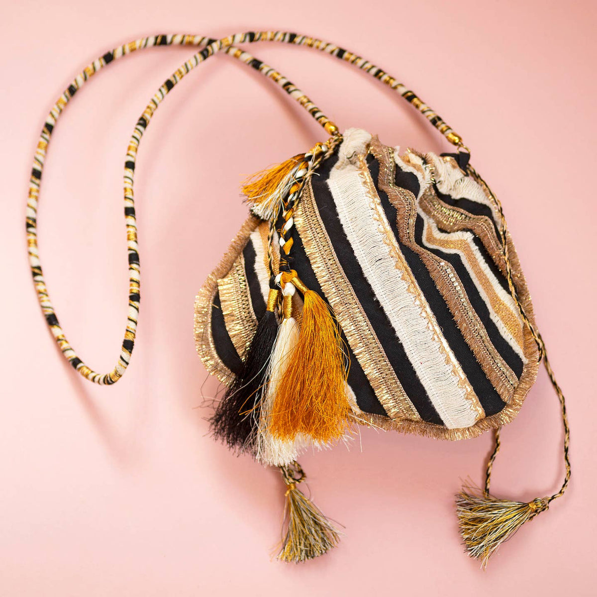 Gorgeous black and gold boho drawstring handbag bursting with textured stripes, shimmering details and playful statement tassels.